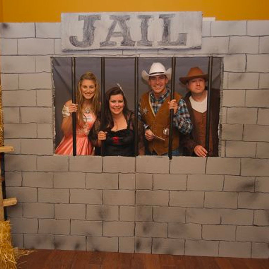 Guests in Wild West costumes posing behind a fake jail prop at a murder mystery party.