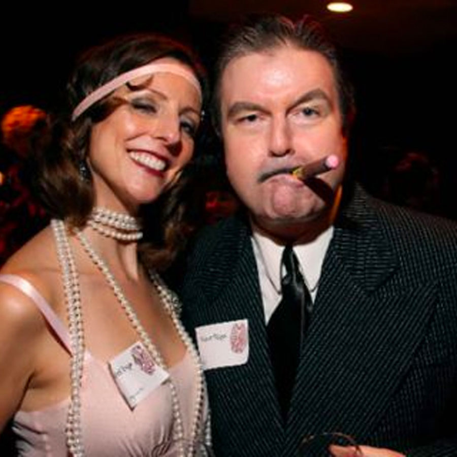 Woman in a flapper dress with pearl necklaces and a man in a pinstripe suit with a fake cigar.