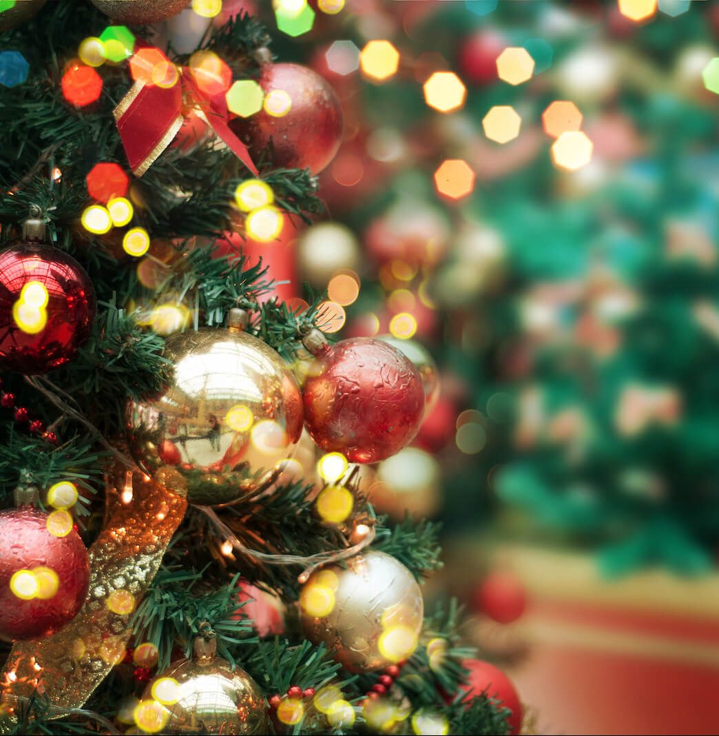 Close-up of a decorated Christmas tree with red and gold ornaments and blurred festive lights.
