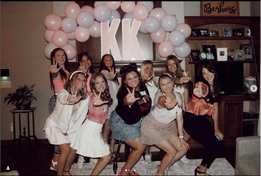 Sorority sisters enjoying a sisterhood murder mystery game, posing playfully with pink balloons in the background.