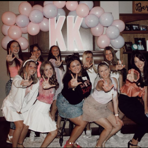 Sorority sisters enjoying a sisterhood murder mystery game, posing playfully with pink balloons in the background.