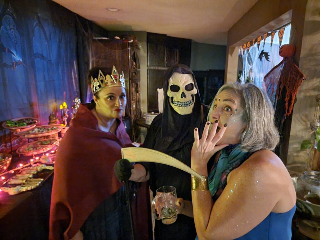 Night of Mystery | Halloween Games For Adults: From Classic Party Hits To Mystery Night Standouts People in costumes posing playfully next to a spooky Halloween-themed buffet setup.
