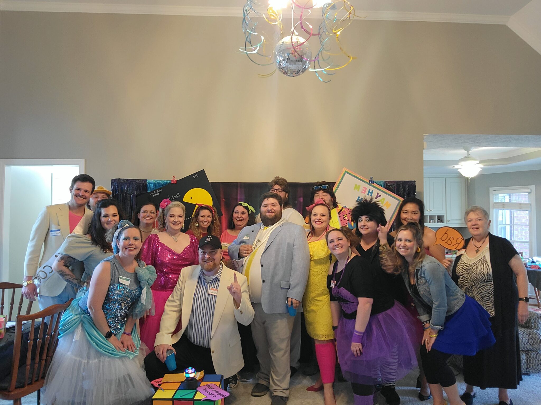 Guests posing together in colorful 1980s costumes in front of a neon prom-themed murder mystery party backdrop