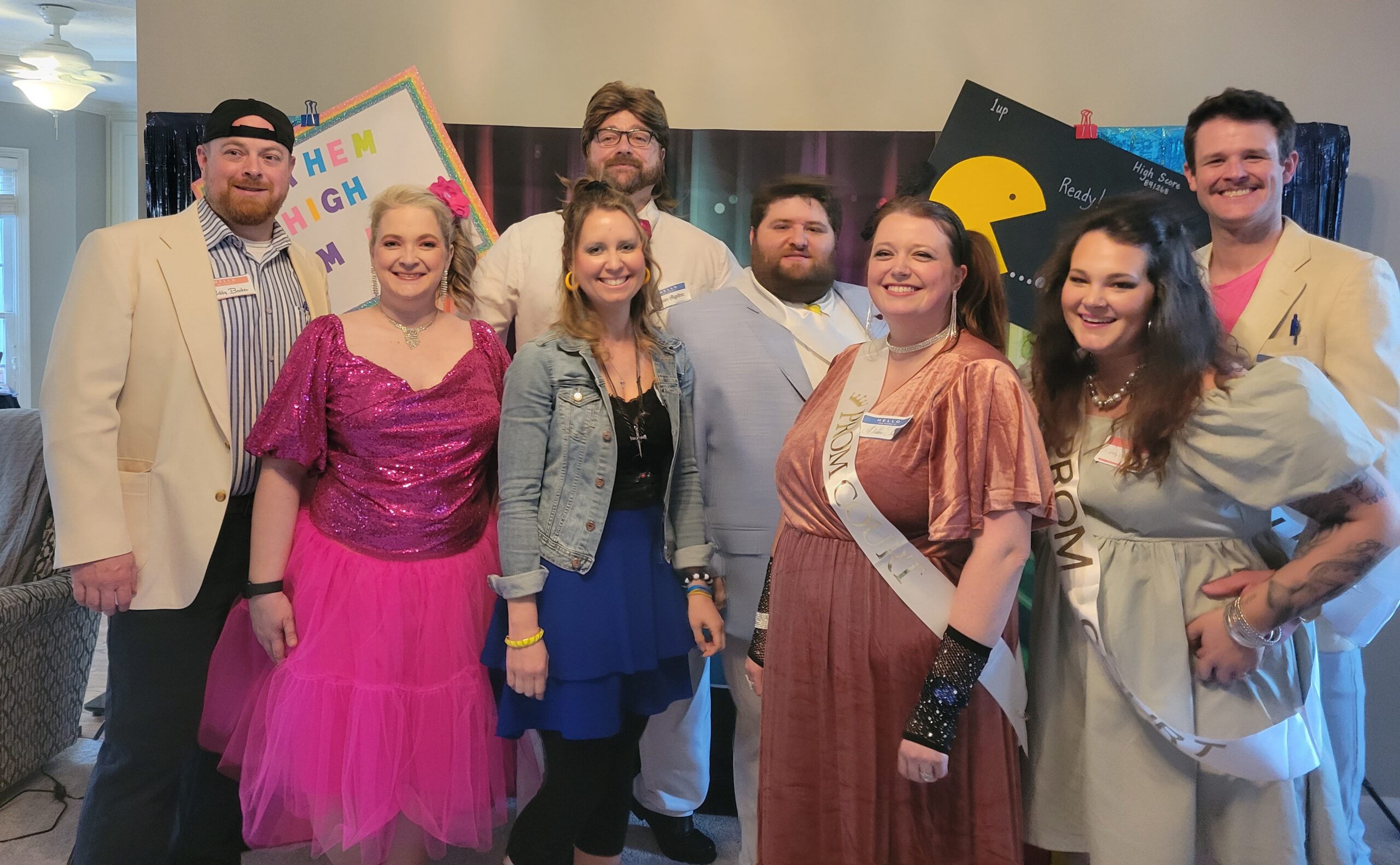 Night of Mystery | Totally Rad 80s Prom Gone Bad: A Birthday Mystery Party Full of Neon, Nostalgia & Nonstop Laughs Guests posing together in colorful 1980s costumes in front of a neon prom-themed murder mystery party backdrop